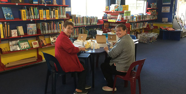 teacher aides creating learning packs in a school library