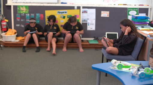 Three students sitting on the floor using iPads and one student sitting on a seat using an iPad