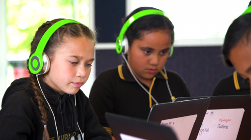 Two students working on laptops wearing green headphones